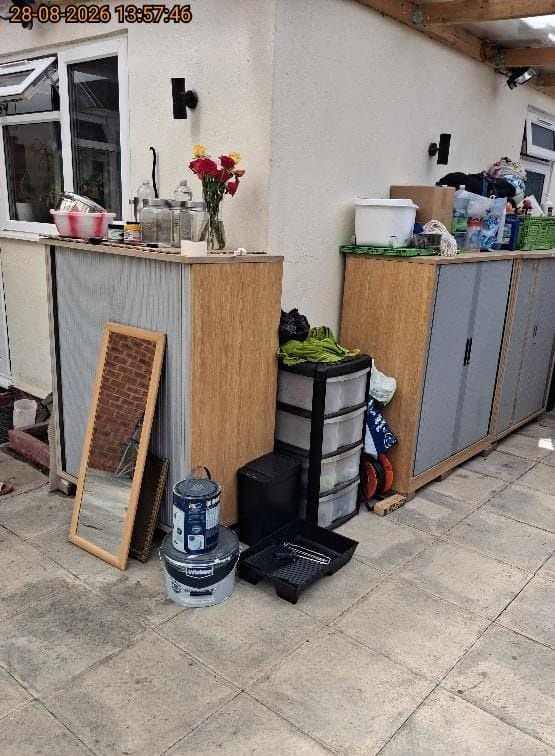 Patio full of household items awaiting clearance including storage drawers, a mirror, cabinets and paint tins