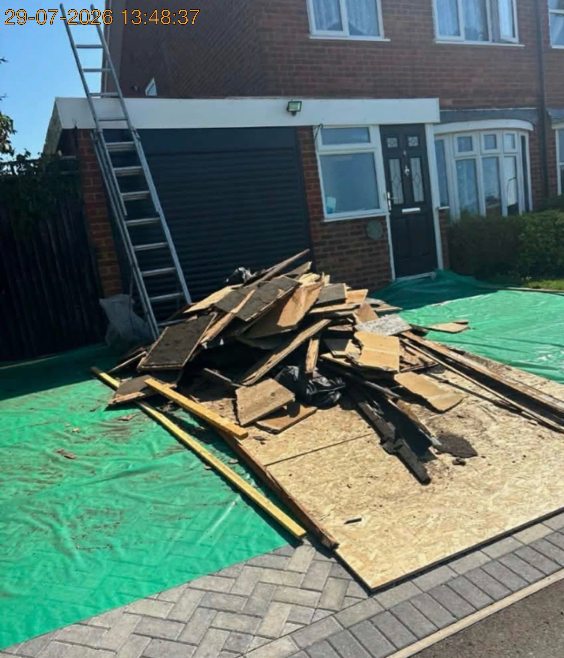 Pile of old roofing boards, timber and felt on a protected driveway on Hazlehurst Drive, Aylesbury, before clearance