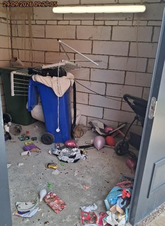 Communal bin store at Arrowsmith Court, Thame, with a dumped pram, clothes airer, balloons, bags and litter across the floor before clearance