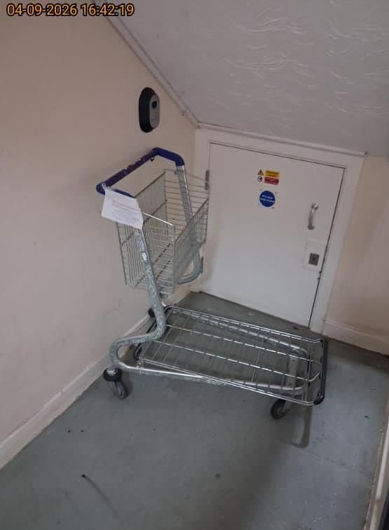 Abandoned metal shopping trolley dumped in a communal stairwell by a fire door before clearance in Watford