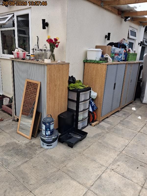 Patio full of household items awaiting clearance including storage drawers, a mirror, cabinets and paint tins